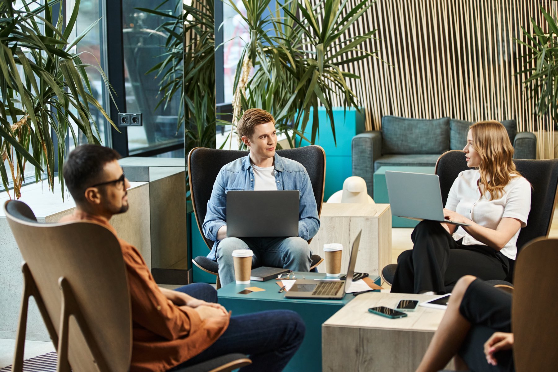 A warm, plant-filled studio workspace where the team collaborates over coffee
